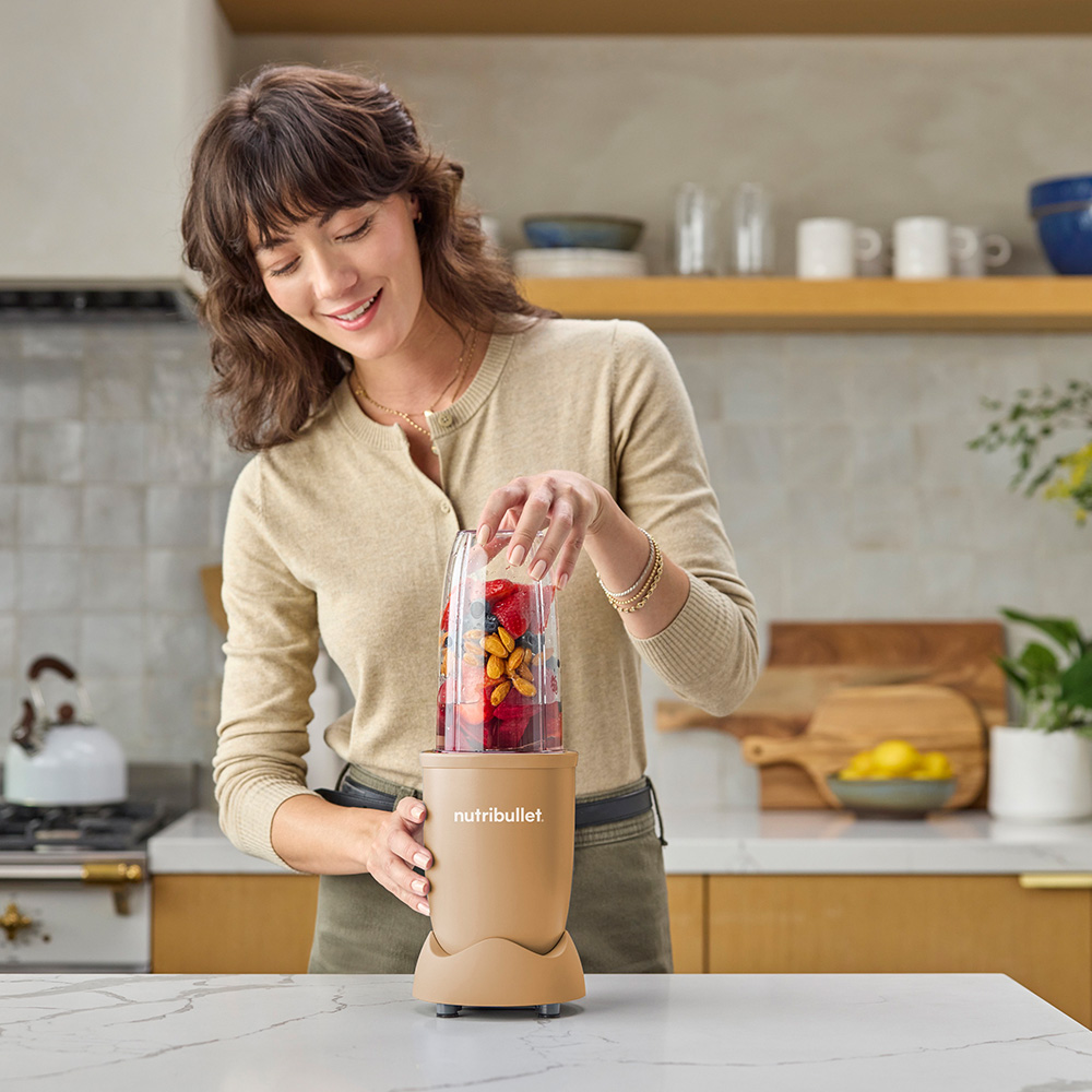 Woman preparing a smoothie with fruits and nuts in a Nutribullet blender.