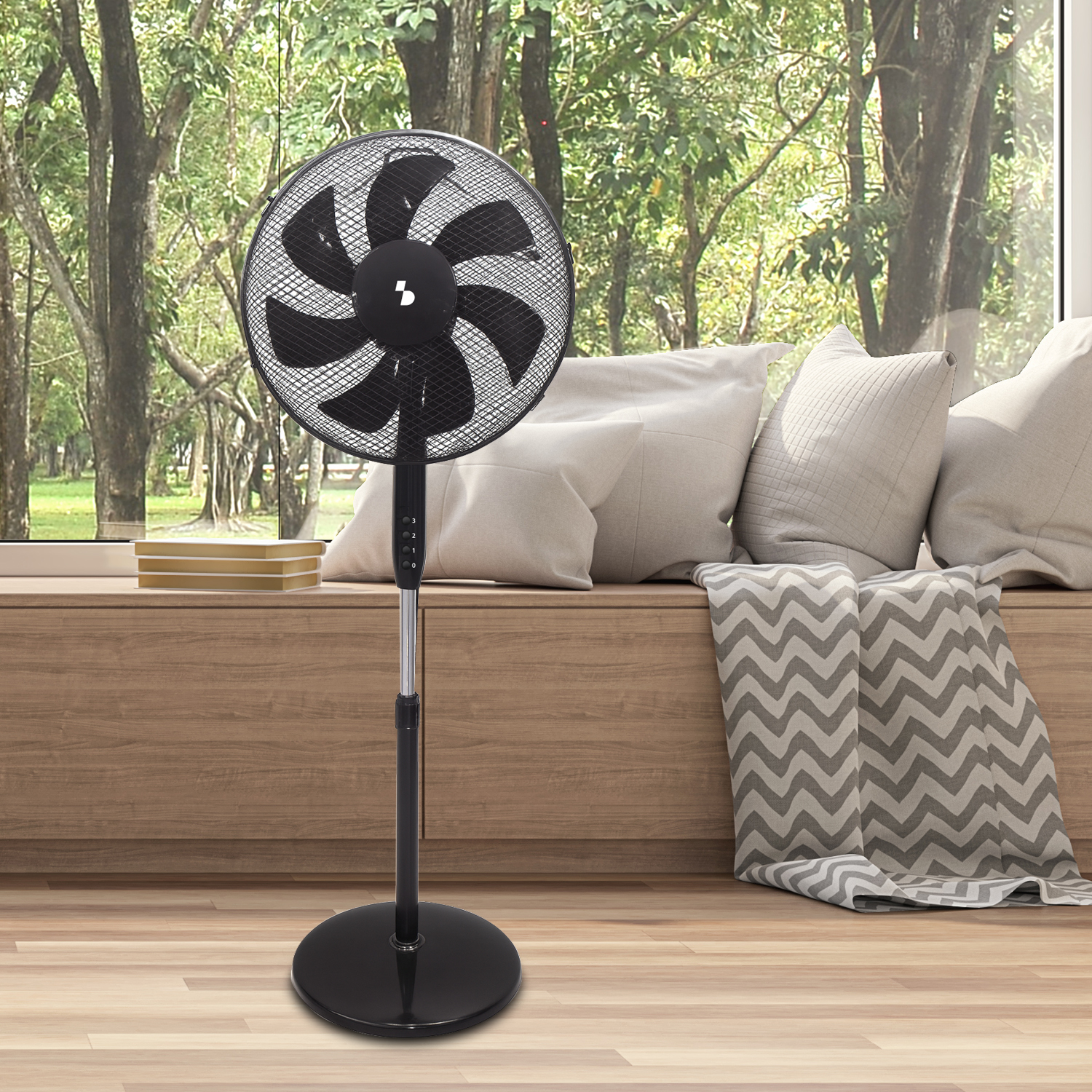 Un ventilatore da terra nero è posto davanti a una finestra con alberi.
