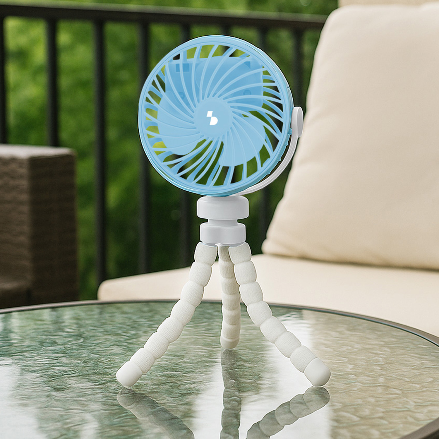 Un mini ventilatore blu con gambe flessibili si trova su un tavolino di vetro.