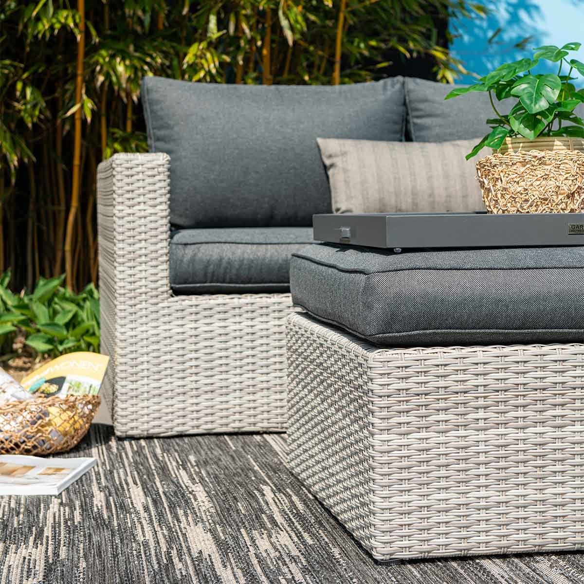 Meubles de jardin gris avec coussins, plateau et plante sur un tapis.