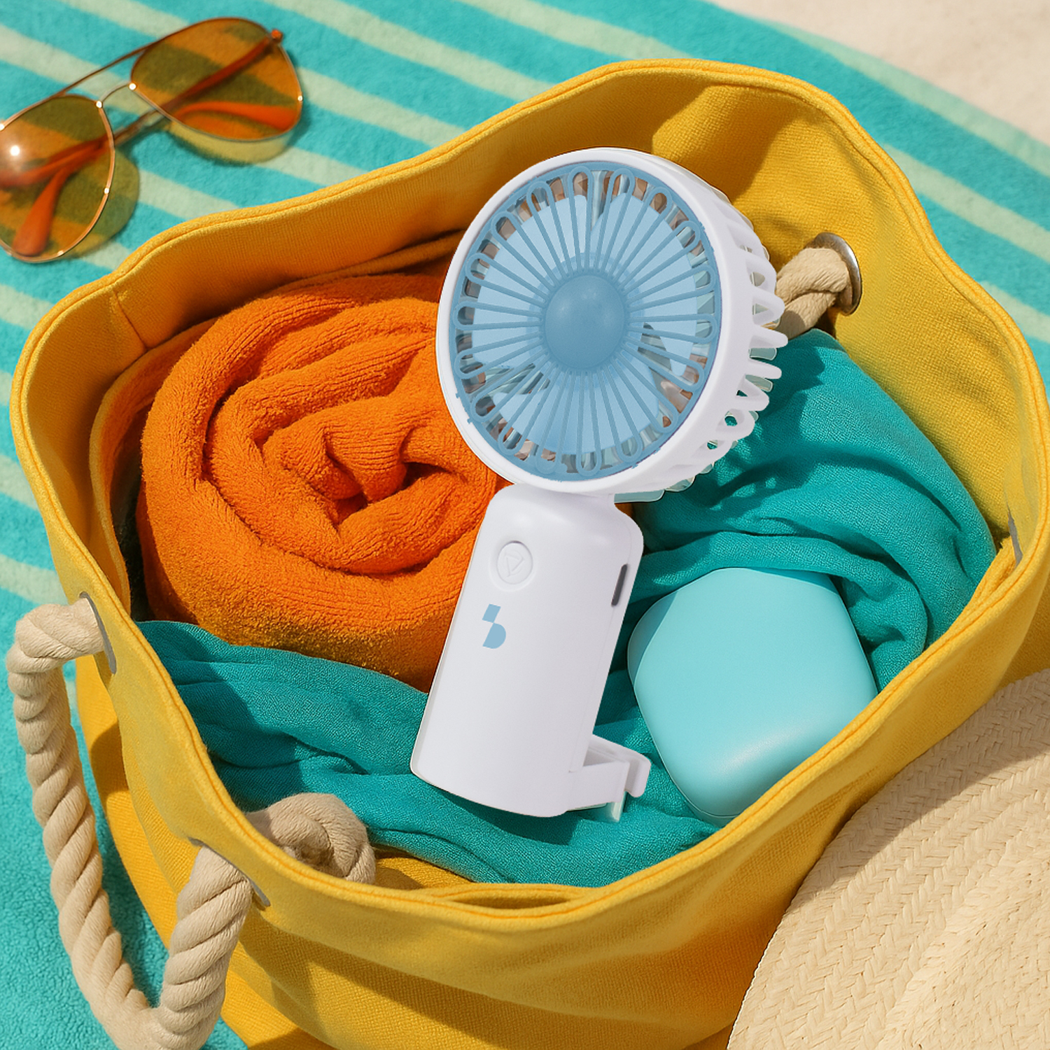 Borsa da spiaggia gialla con asciugamano arancione arrotolato, tessuto verde acqua, ventilatore.
