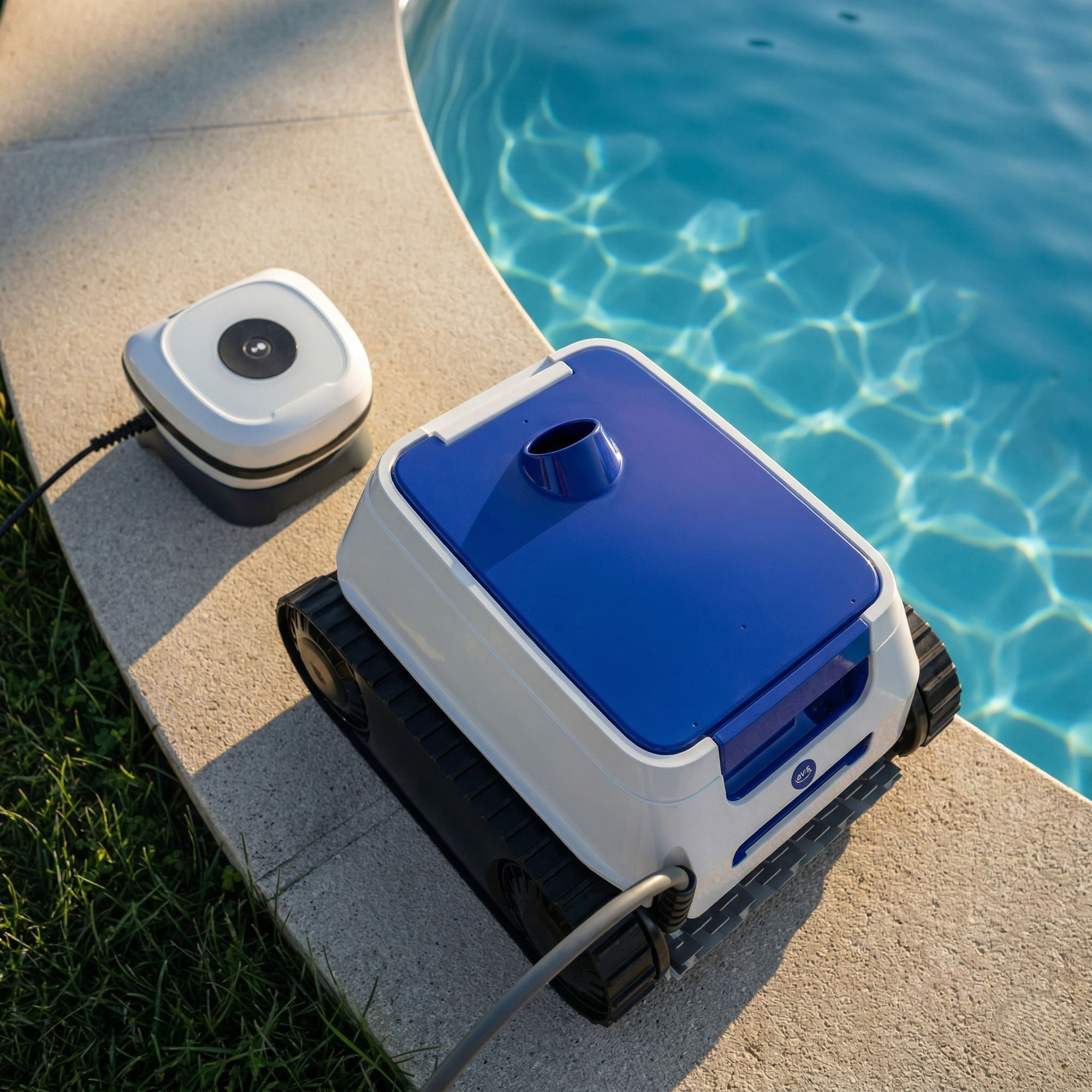 Un robot limpiafondos azul y blanco con orugas está en el borde de la piscina junto a una fuente de alimentación.