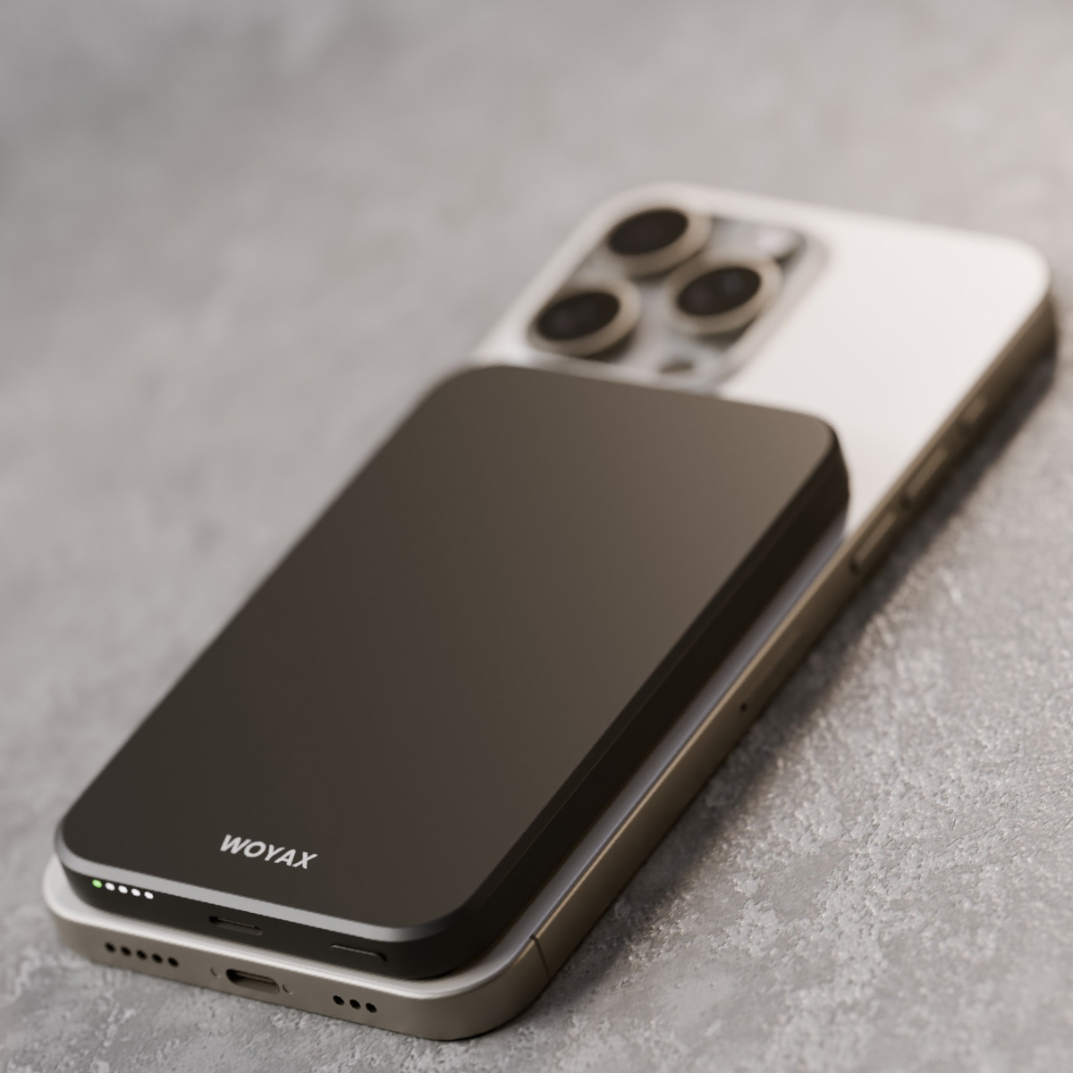 Koyu gri Woyax powerbank, gri yüzeyde gümüş bir akıllı telefonun üzerinde duruyor.