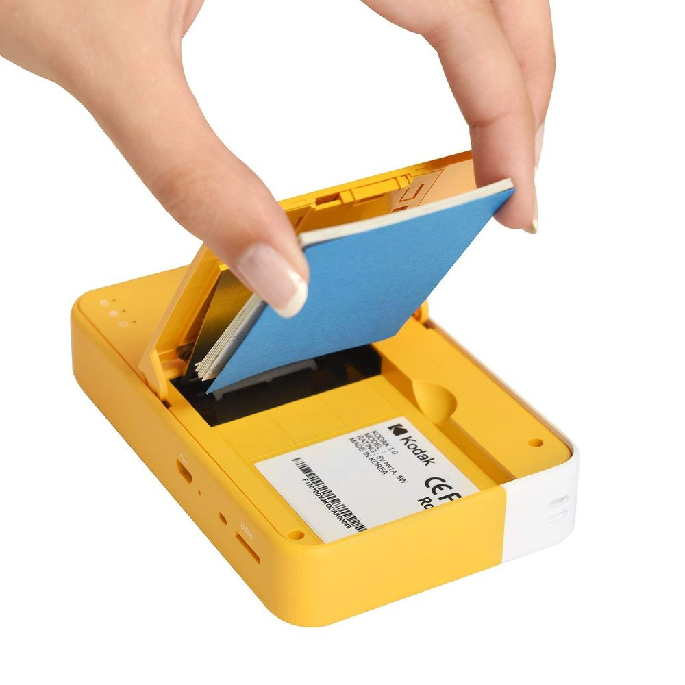 Eine Hand setzt eine blaue Papierkassette in einen gelben Kodak-Drucker.