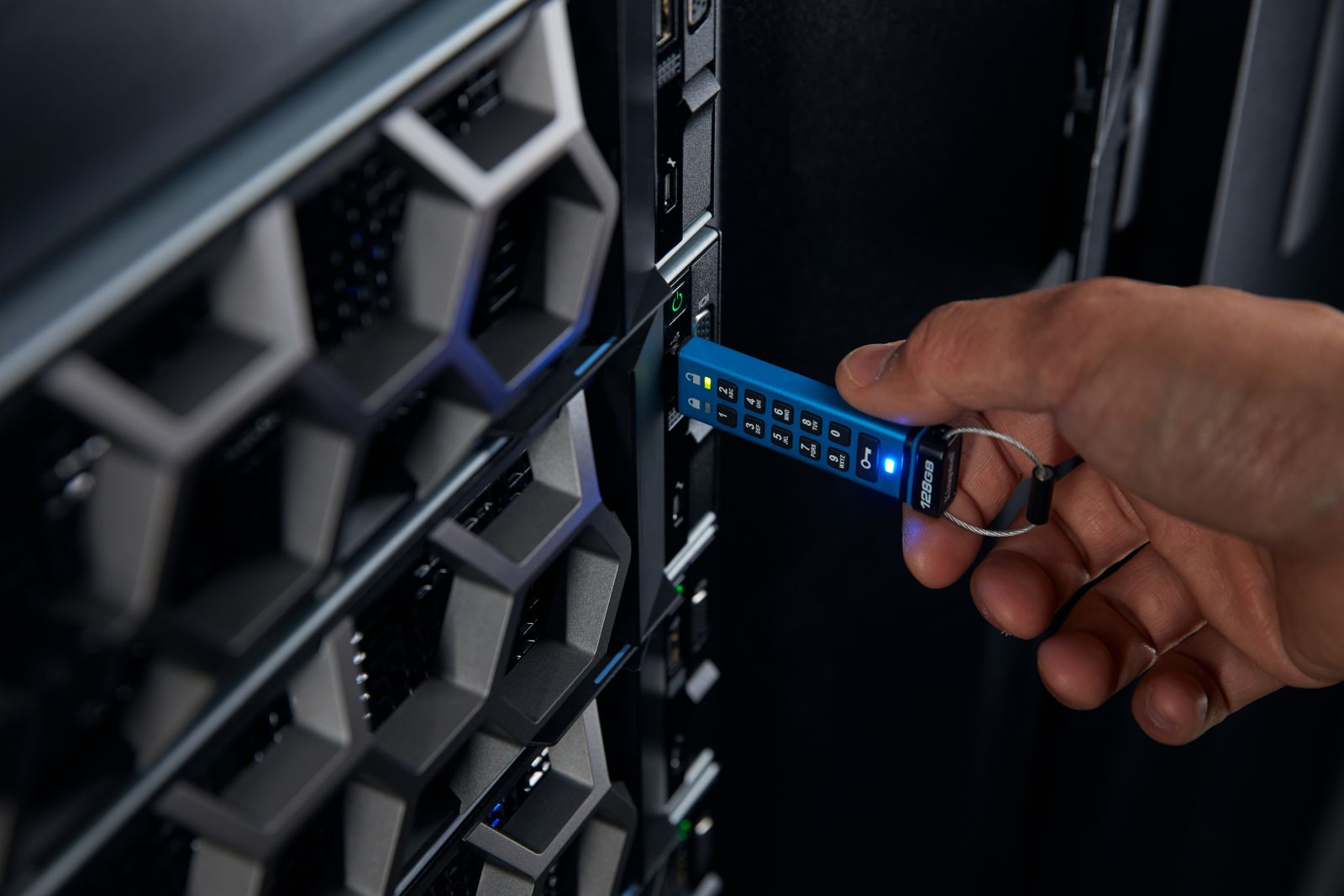Eine Hand steckt einen blauen USB-Stick mit Tastatur in einen Server.