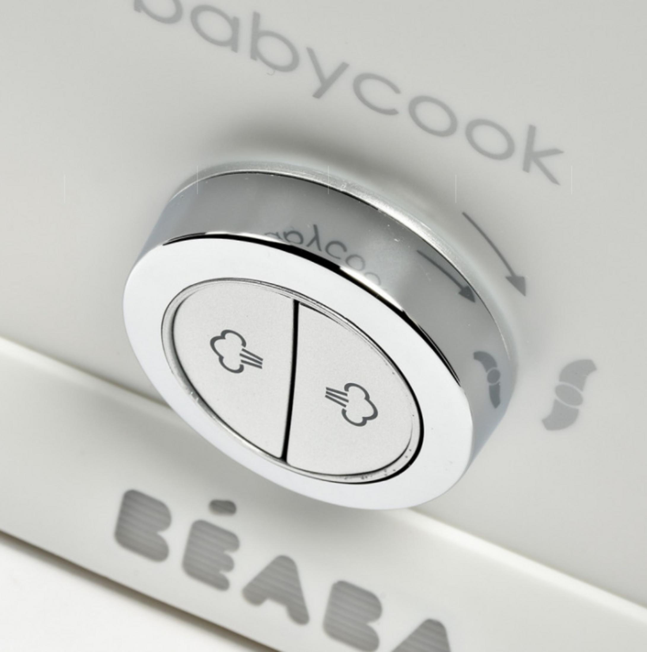 Nahaufnahme eines weißen Babykost-Geräts mit einem Chromknopf und Dampfsymbolen.