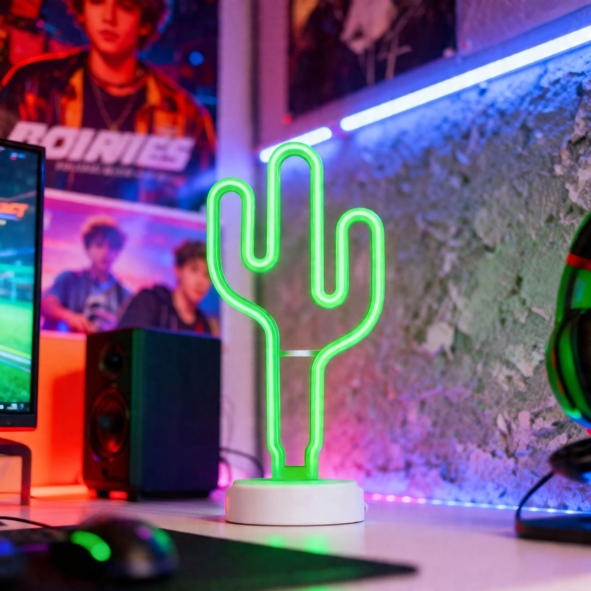 Een groene neon cactuslamp staat op een bureau met een computermonitor en koptelefoon.