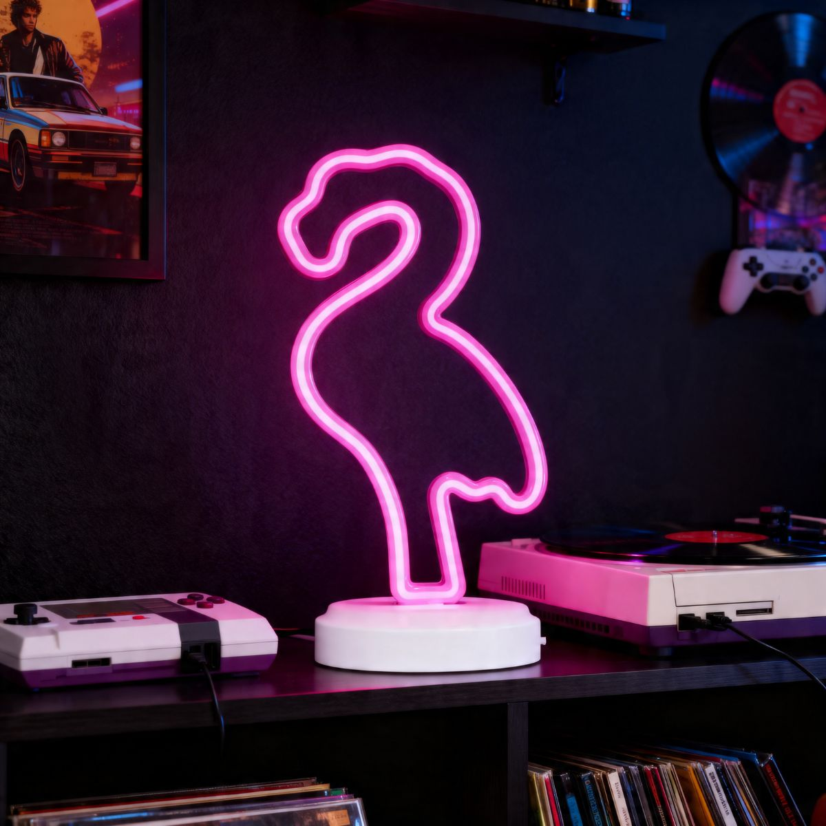 Een roze neon flamingo lamp gloeit op een plank met retro gameconsoles en een platenspeler.