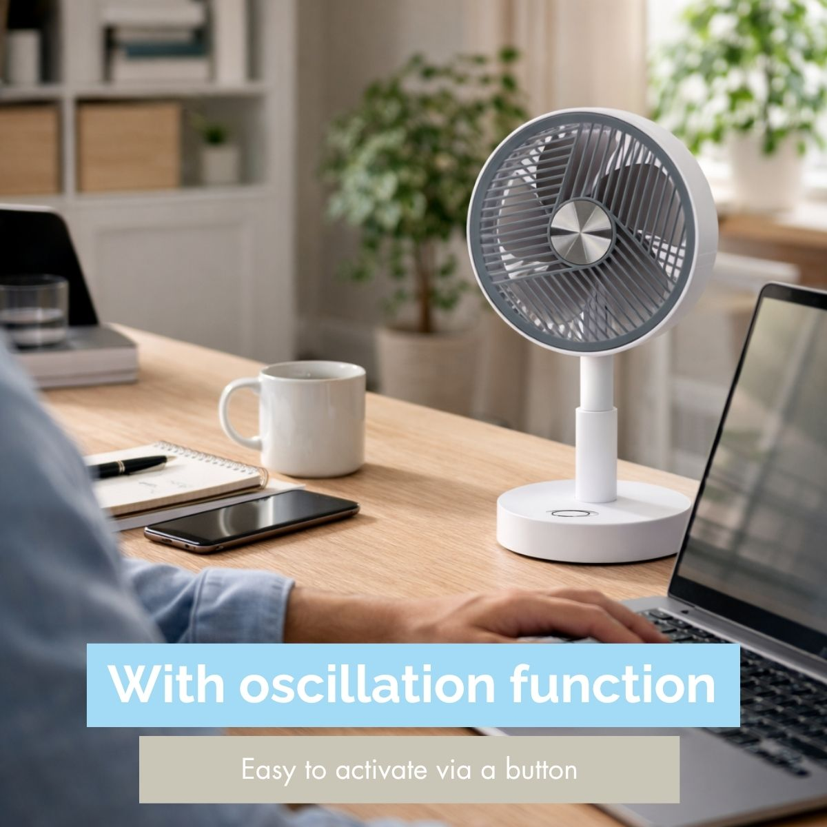 A white fan sits on a desk next to a mug and a laptop.