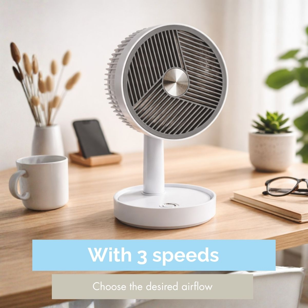 A white desk fan sits on a wooden table with a mug and phone nearby.