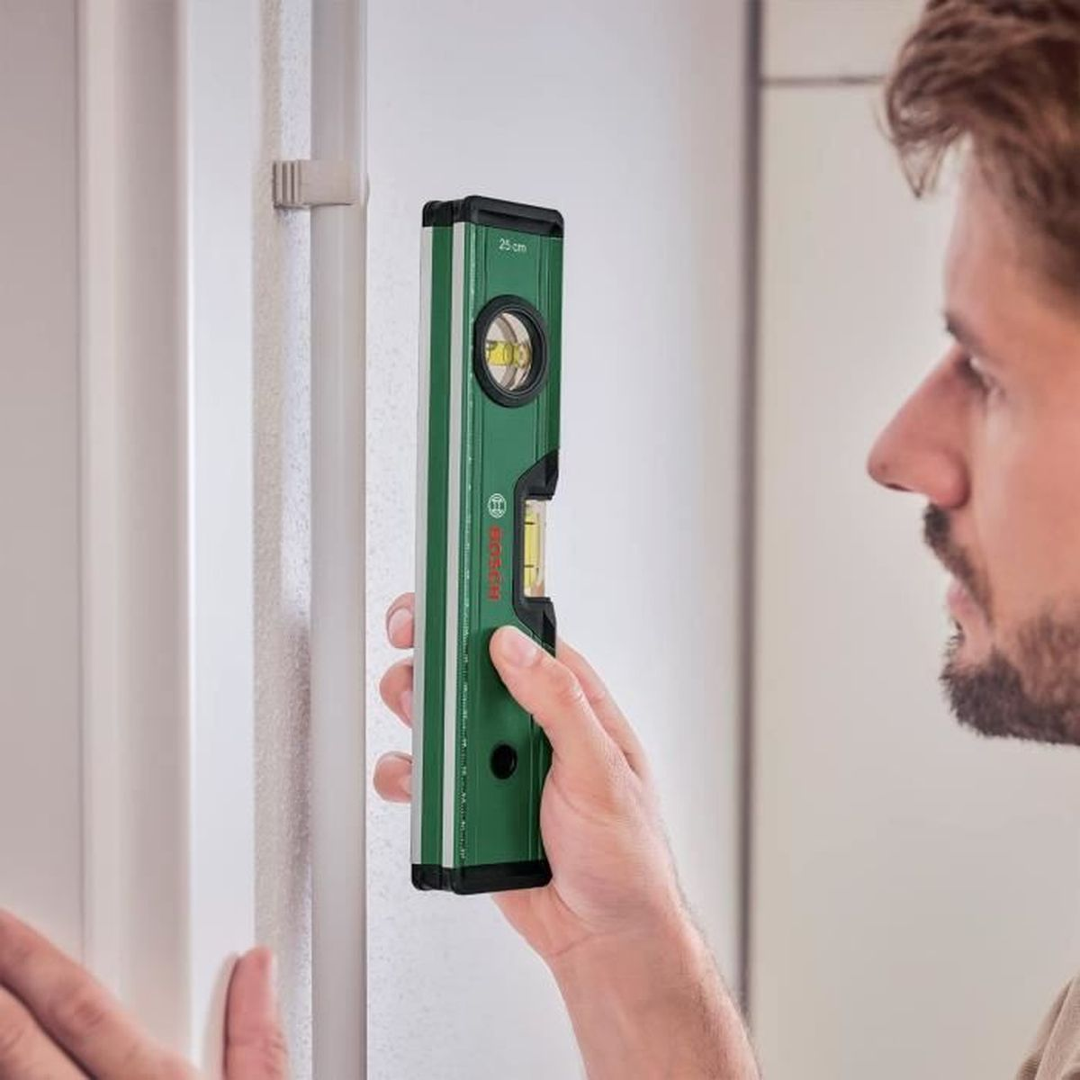 Ein Mann hält eine grüne Wasserwaage an eine weiße Wand.