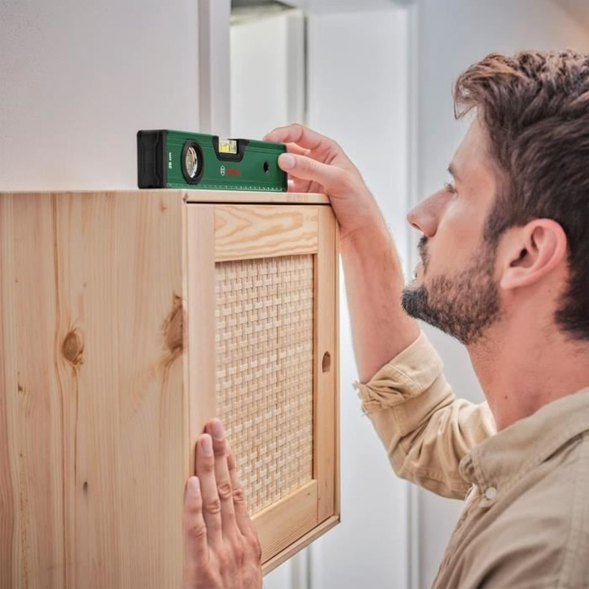 Mann benutzt eine grüne Bosch-Wasserwaage, um zu prüfen, ob ein Holzschrank eben ist.