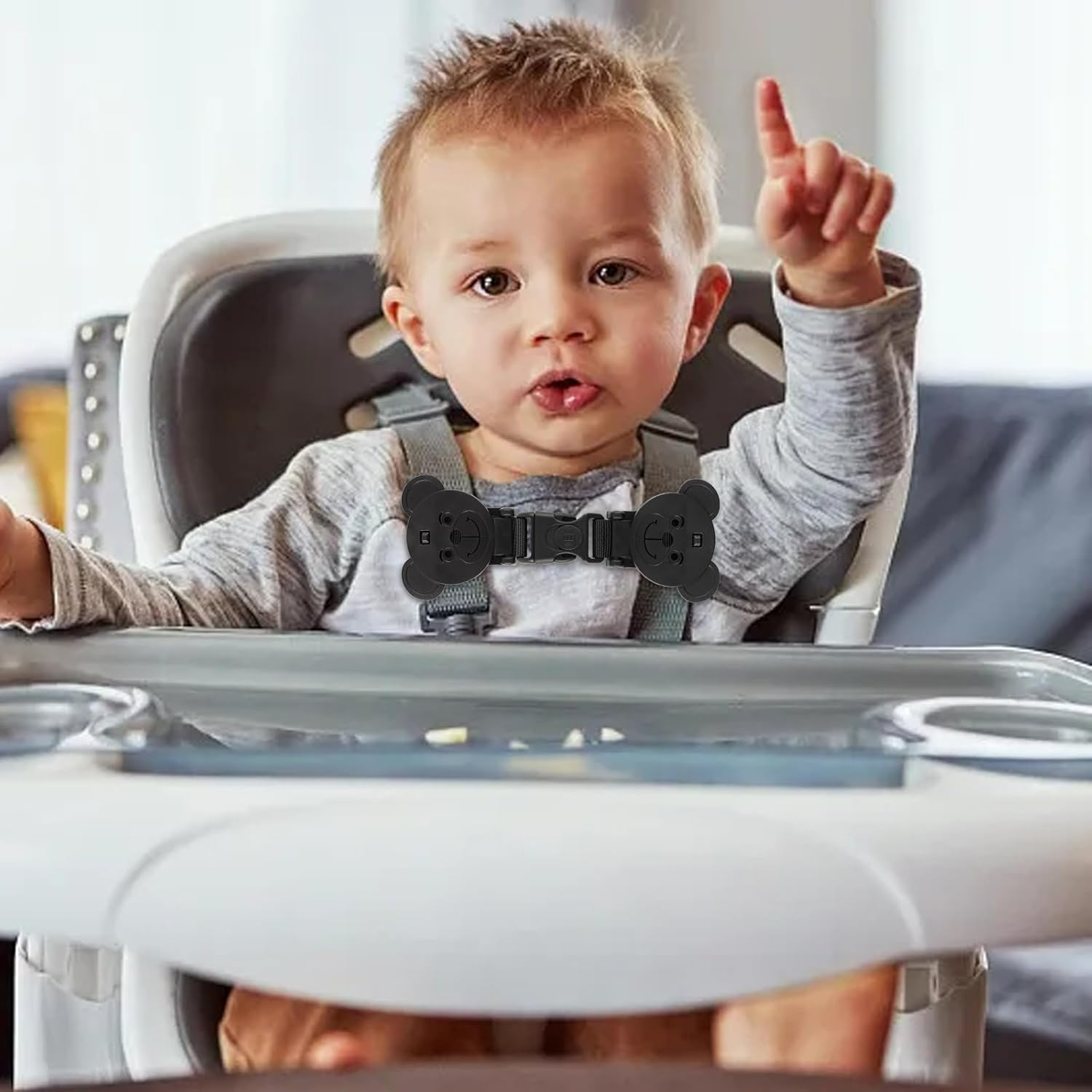 Ein Baby sitzt in einem Hochstuhl mit einem schwarzen Schnallenverschluss mit Teddybärenmotiv.