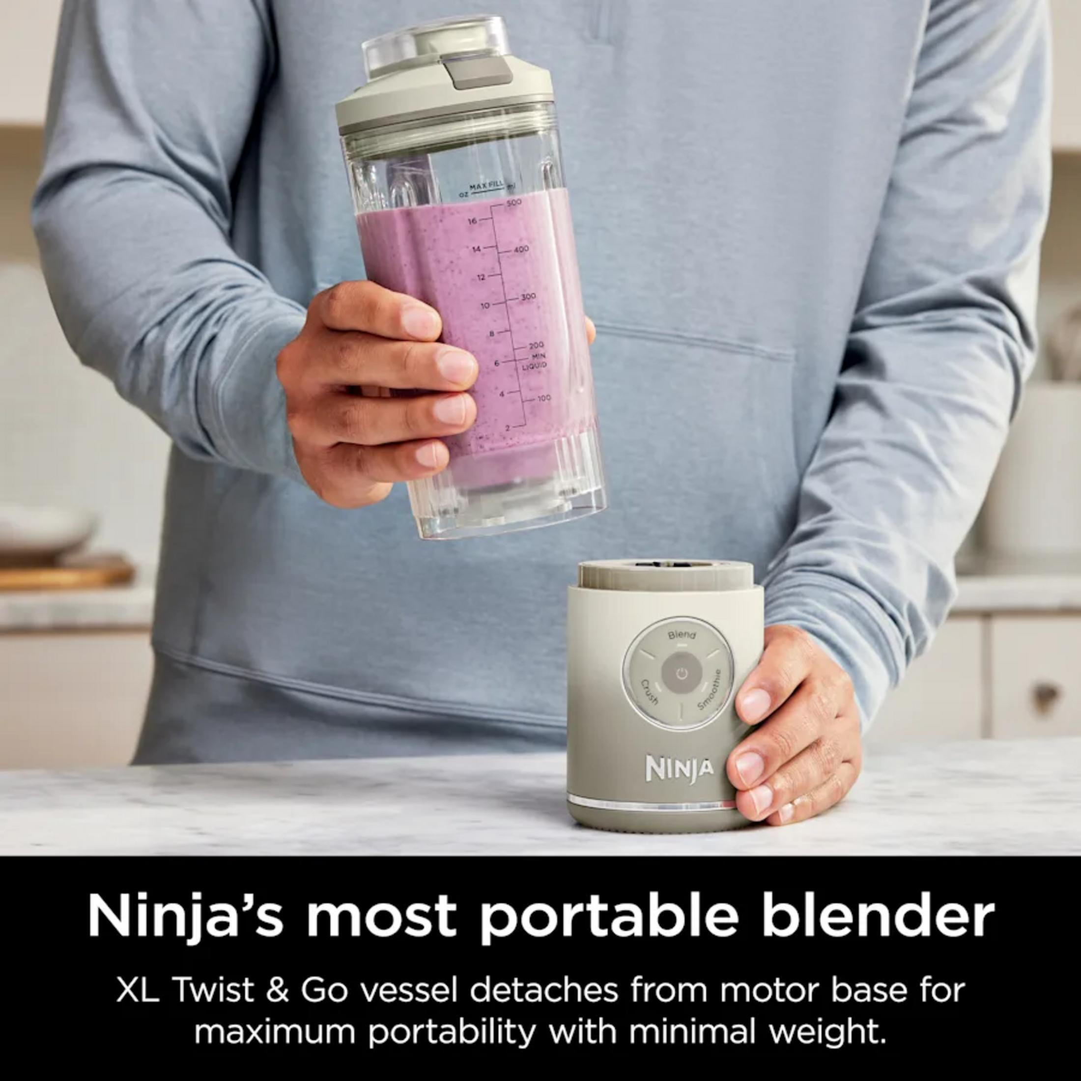 Eine Person hält einen Becher mit einem violetten Smoothie über eine graue Mixereinheit.