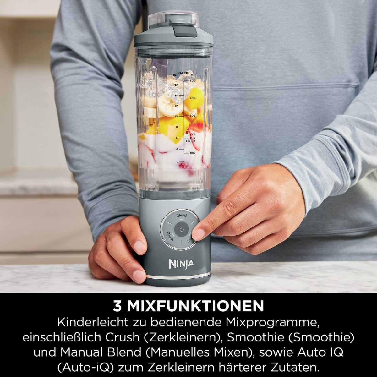 Ein Ninja Blender mit Früchten und Eis, eine Hand drückt den Knopf.