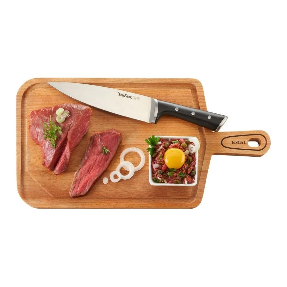 Carne cruda, cuchillo, aros de cebolla y plato con yema de huevo en tabla madera.
