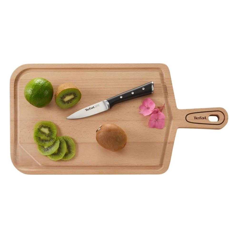 Un cuchillo descansa sobre una tabla de madera junto a kiwis cortados y enteros y una lima.