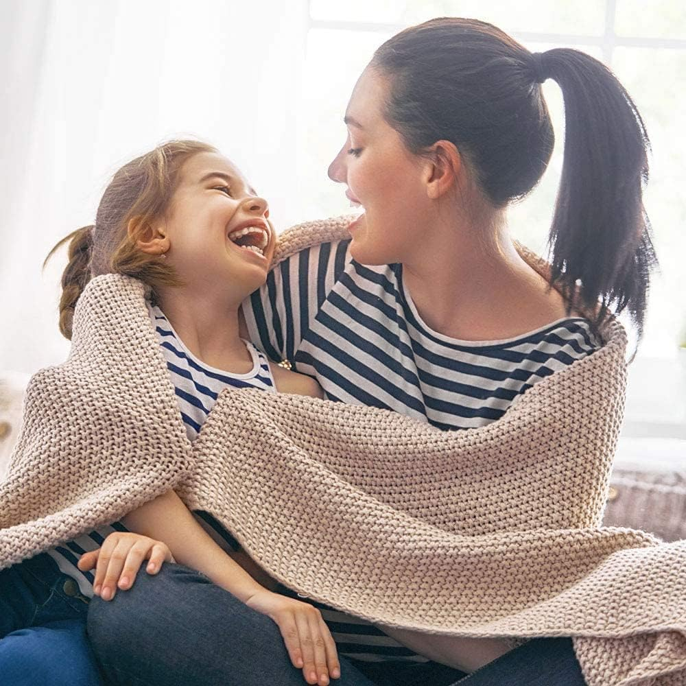 Mutter und Tochter kuscheln sich in eine Decke und lachen.