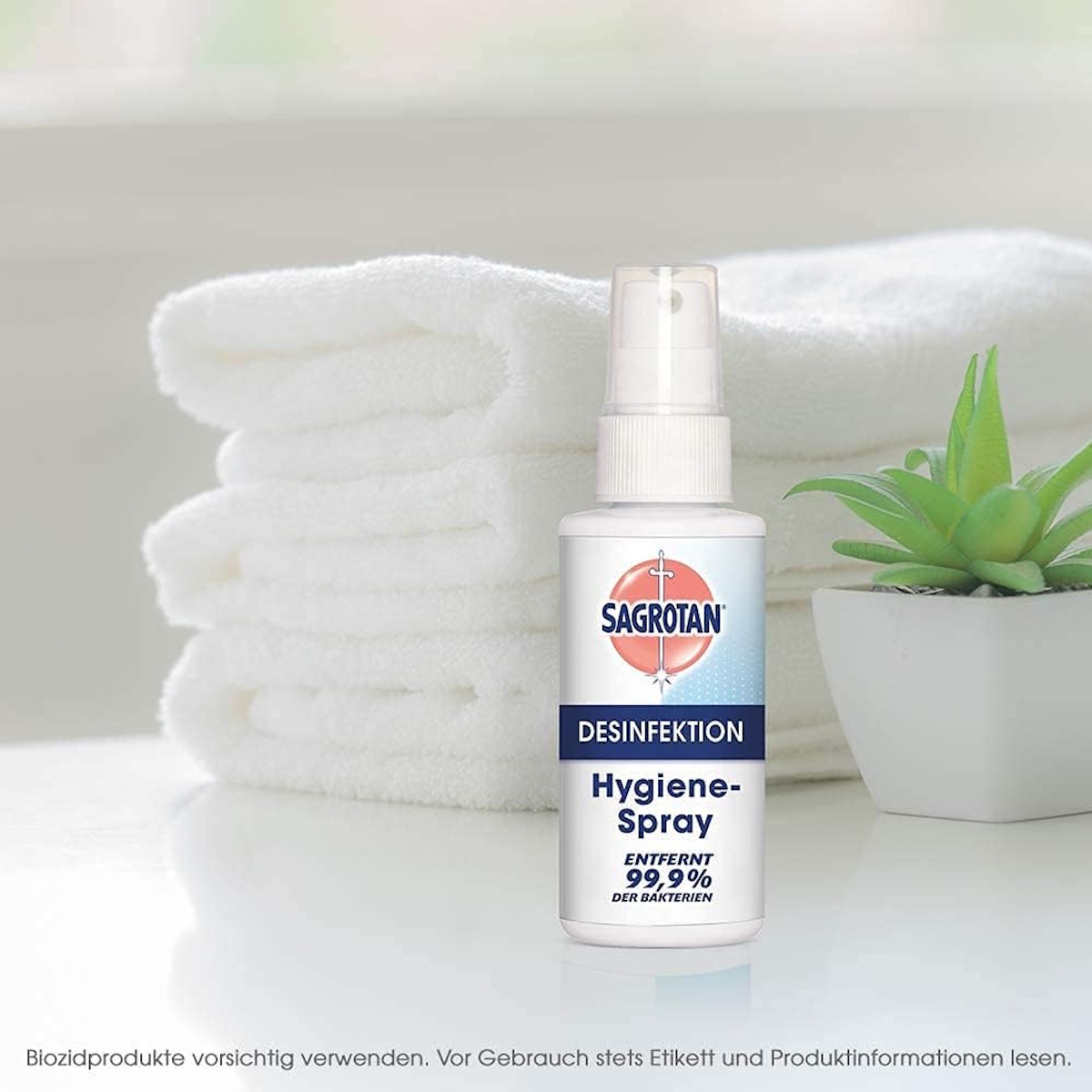 Sagrotan Hygiene Spray Flasche neben weißen Handtüchern und einer Pflanze.