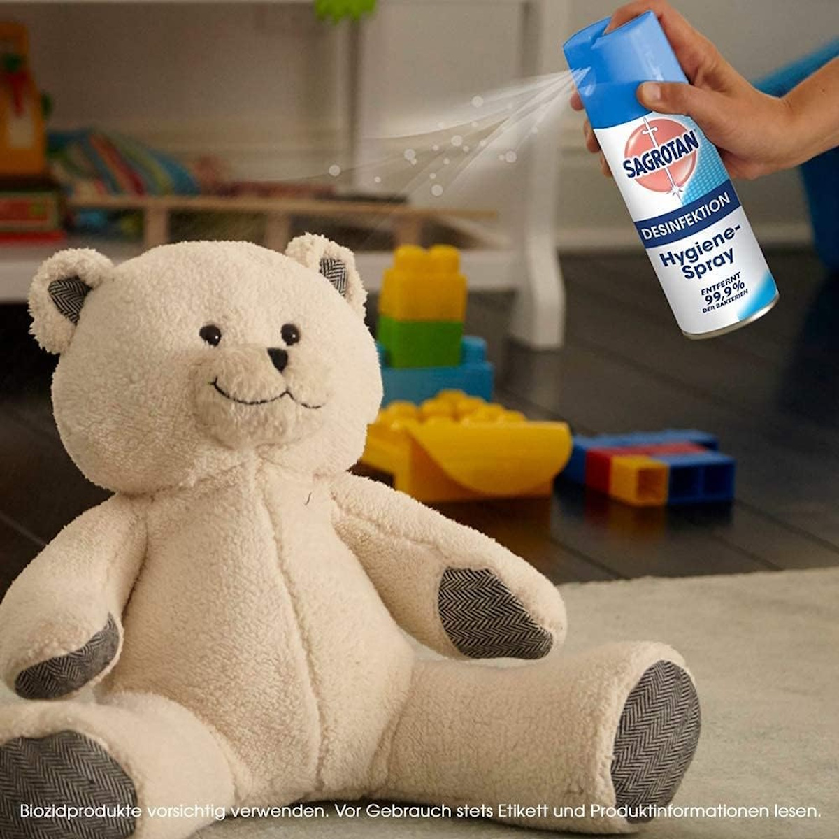 Ein Teddybär sitzt auf dem Boden, während eine Hand Sagrotan Hygiene-Spray sprüht.