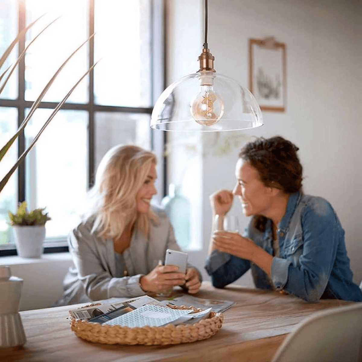 Deux femmes discutent à une table en bois avec une lampe suspendue au-dessus.