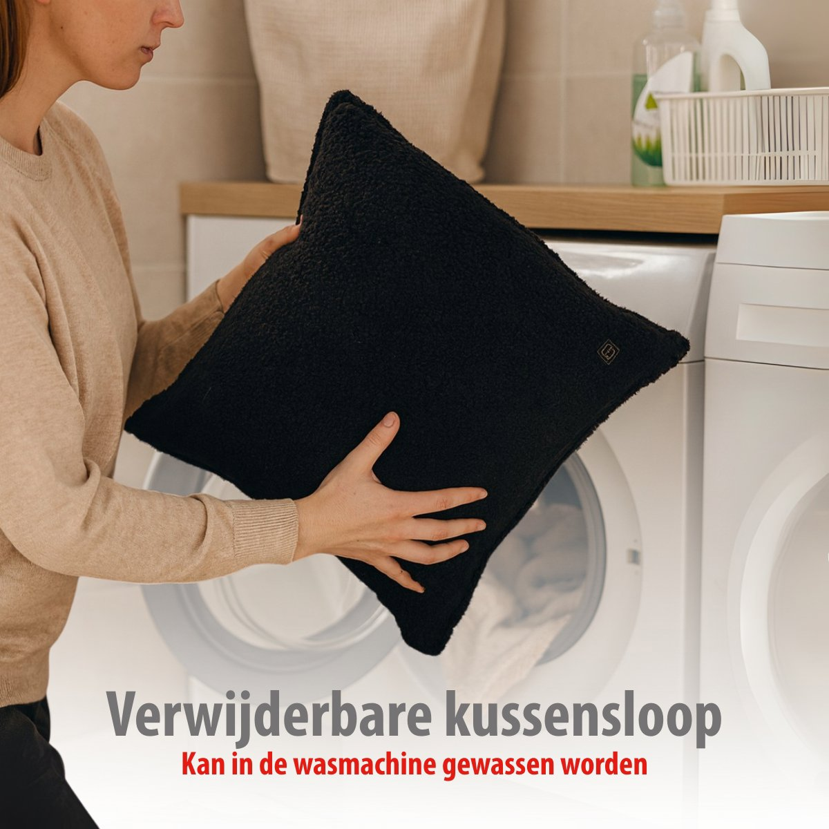 A person holds a black cushion in front of a washing machine.