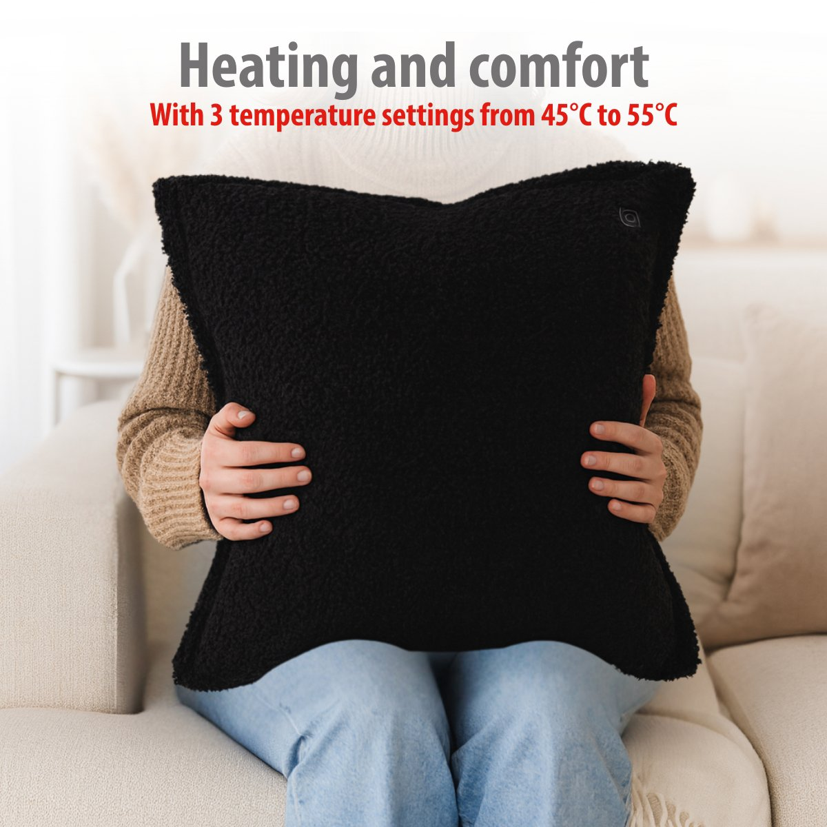 Person holding a black, fuzzy heated pillow while sitting on a couch.