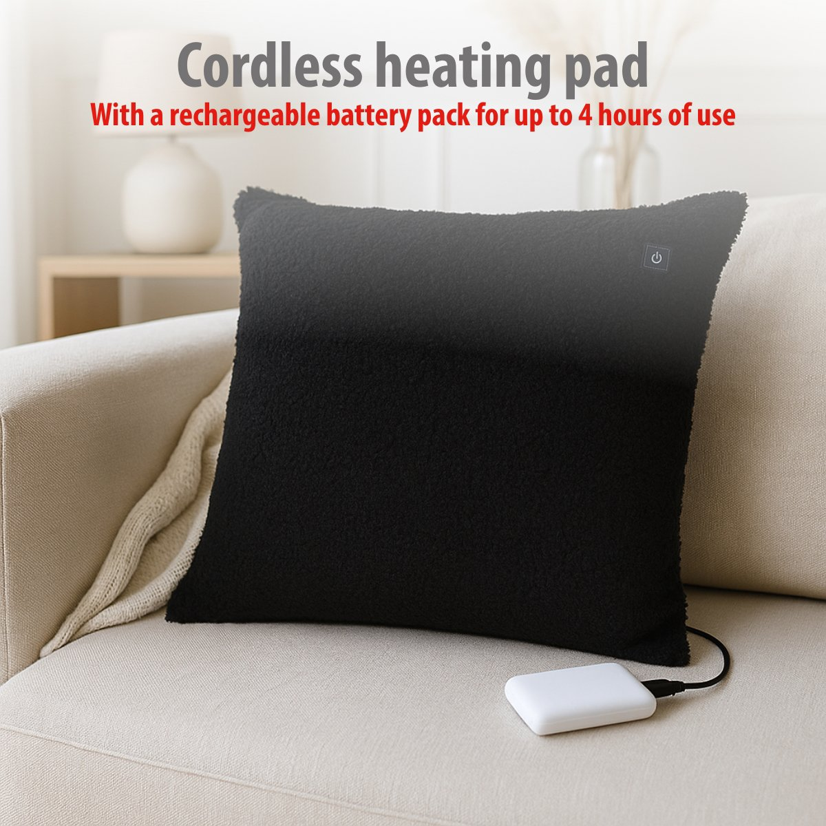 A black cordless heating pad with a power button sits on a sofa, connected to a white battery pack.