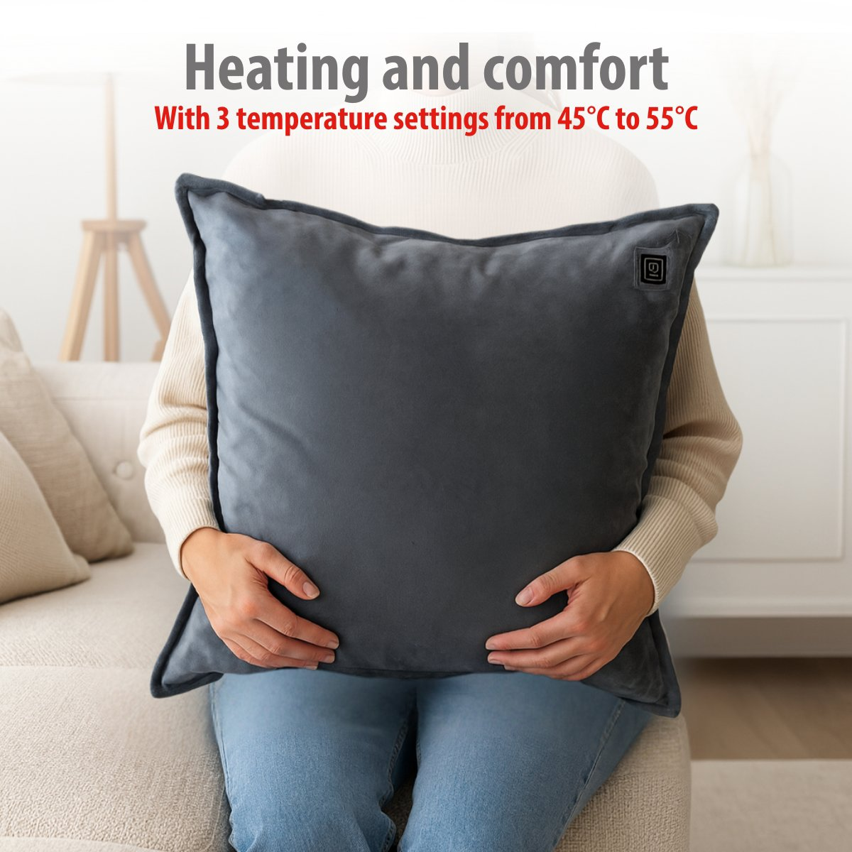 A person holds a dark gray heated pillow with a power symbol on it.