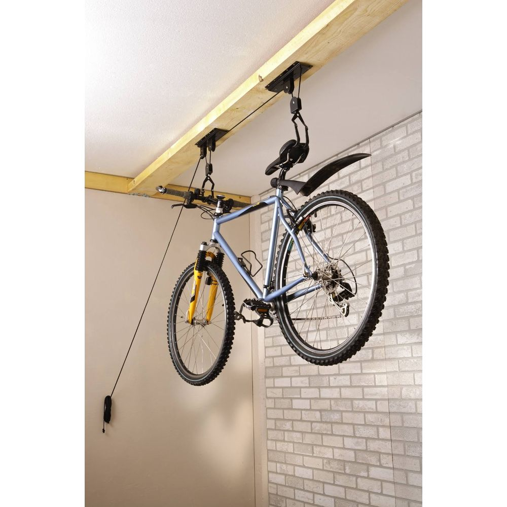 Un vélo bleu est suspendu à un système de palan de plafond fixé à une poutre en bois.