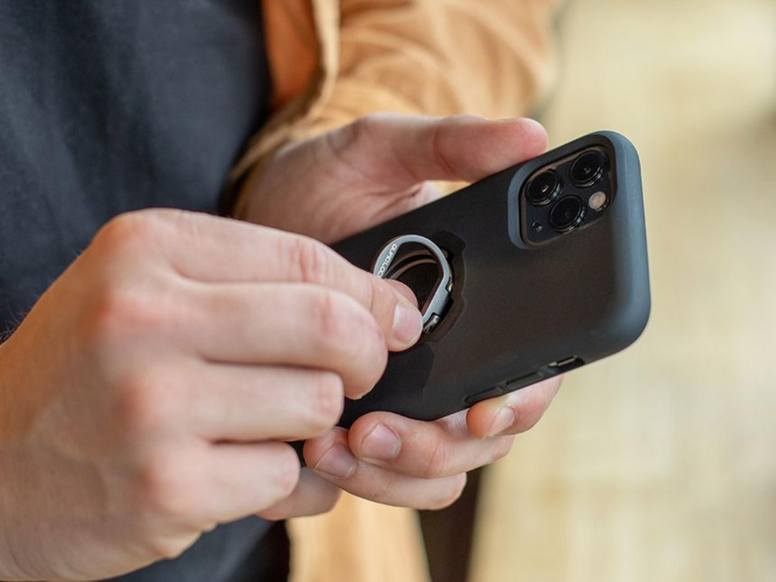 Hände halten ein schwarzes Smartphone mit Ringhalterung.