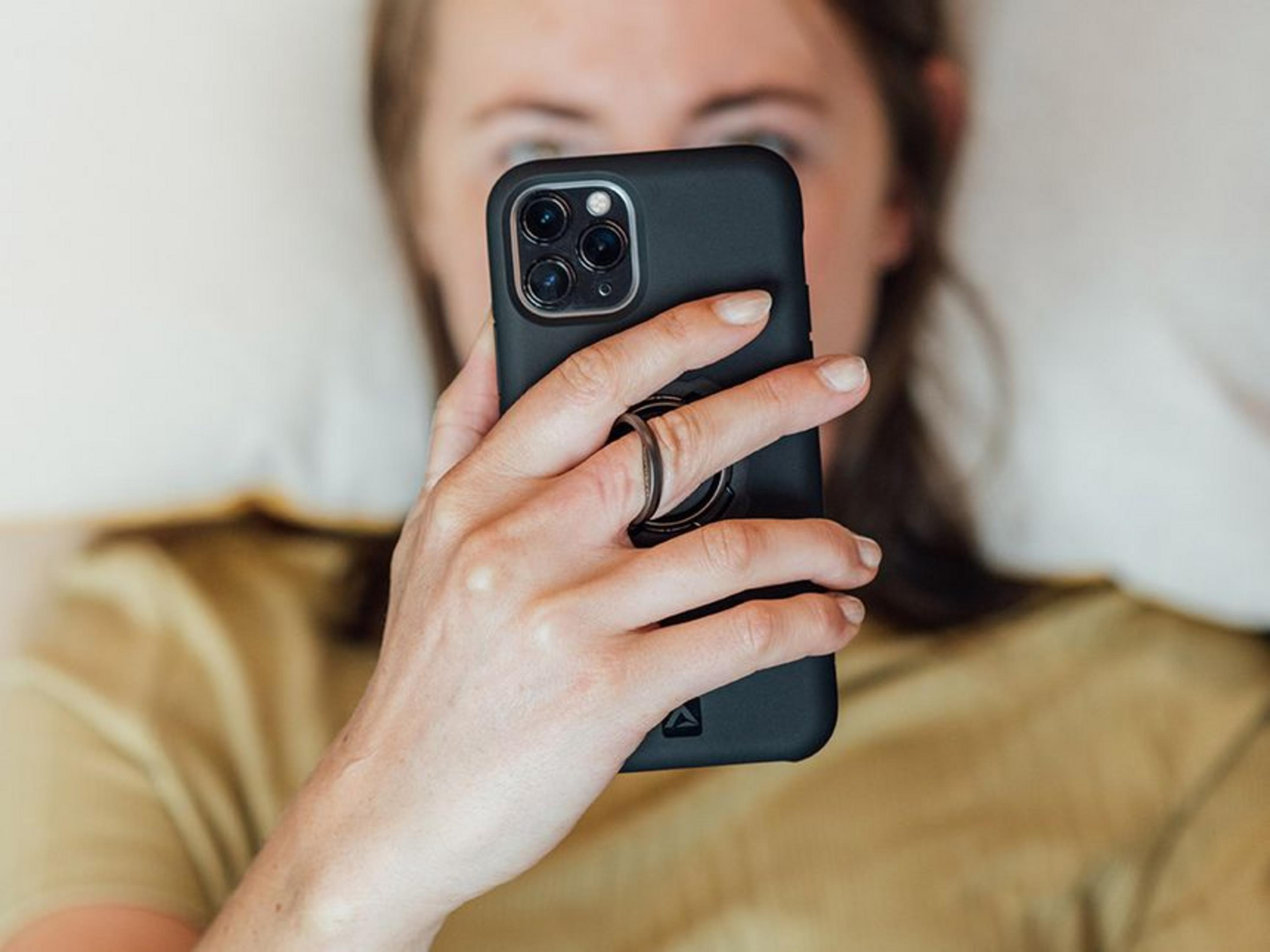 Eine Person hält ein Smartphone mit drei Kameras und einem Ringhalter.