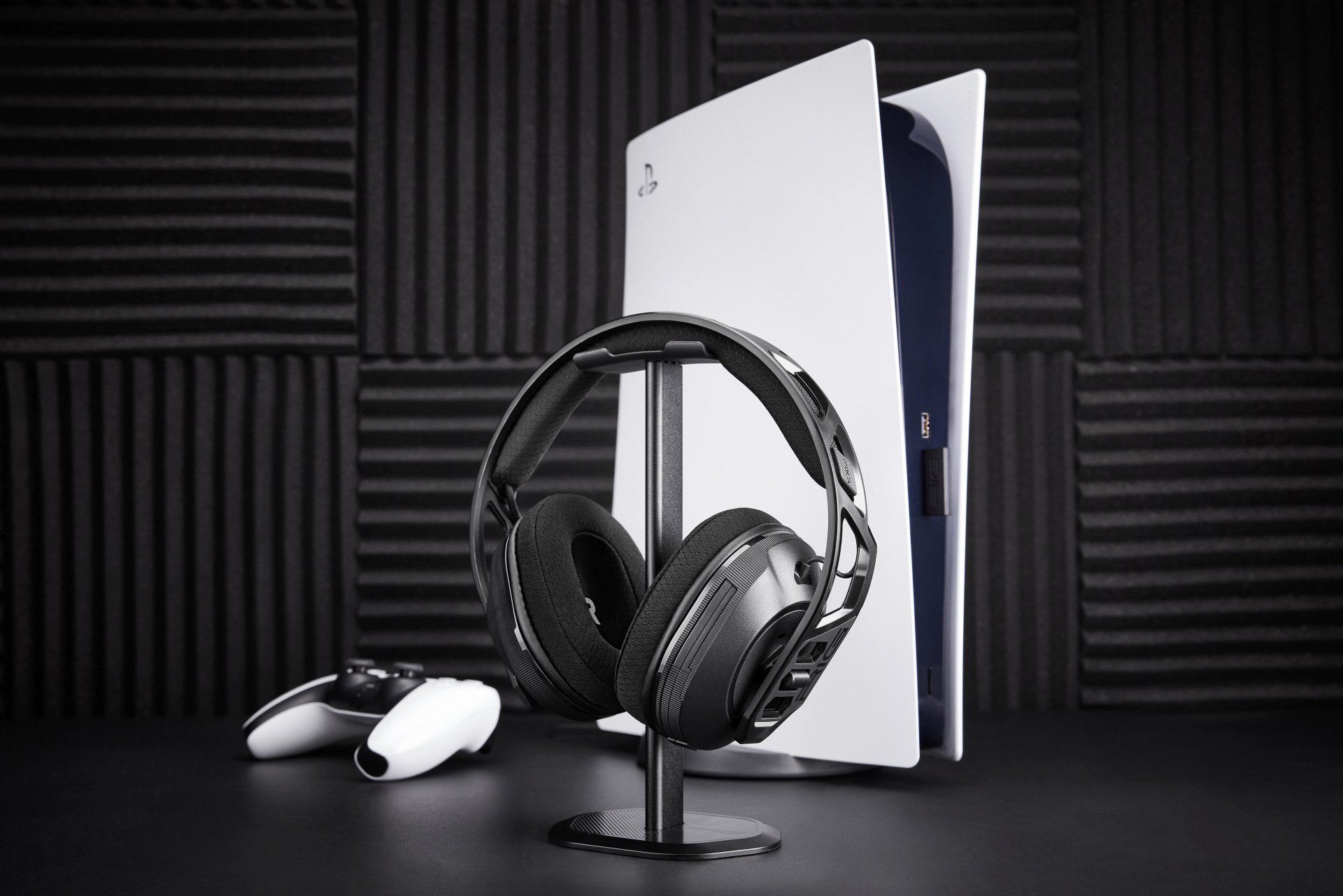 Czarne słuchawki na stojaku przed PlayStation 5 i kontrolerem.