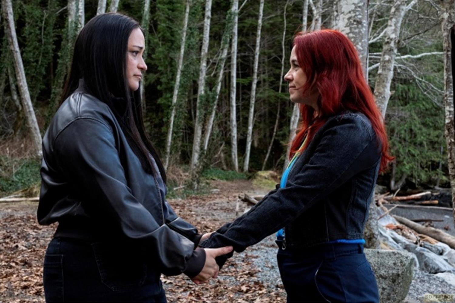 Due donne si tengono per mano in una foresta. Una ha i capelli neri, l'altra rossi.