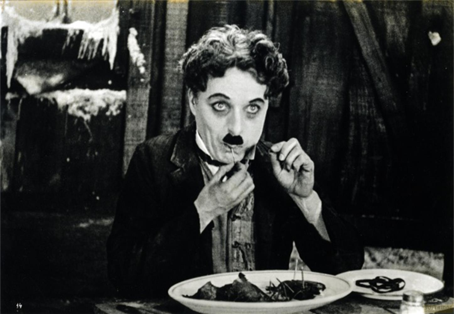 Charlie Chaplin mangia, usando una forchetta per maneggiare il suo cibo.