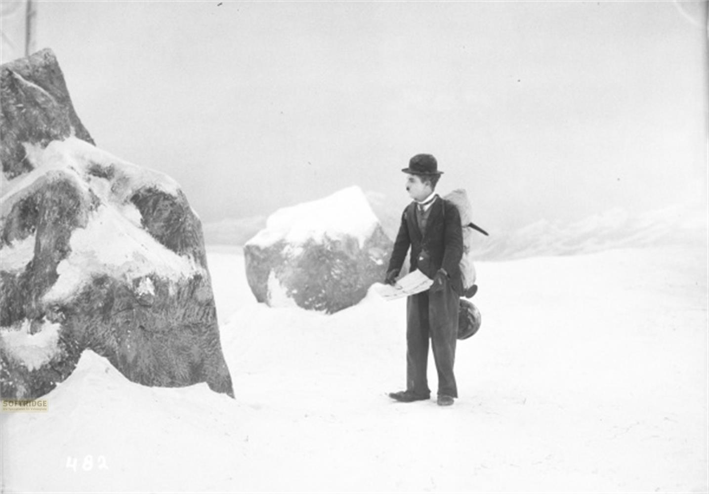 Un uomo in abito e cappello sta in piedi nella neve con zaino e mappa.