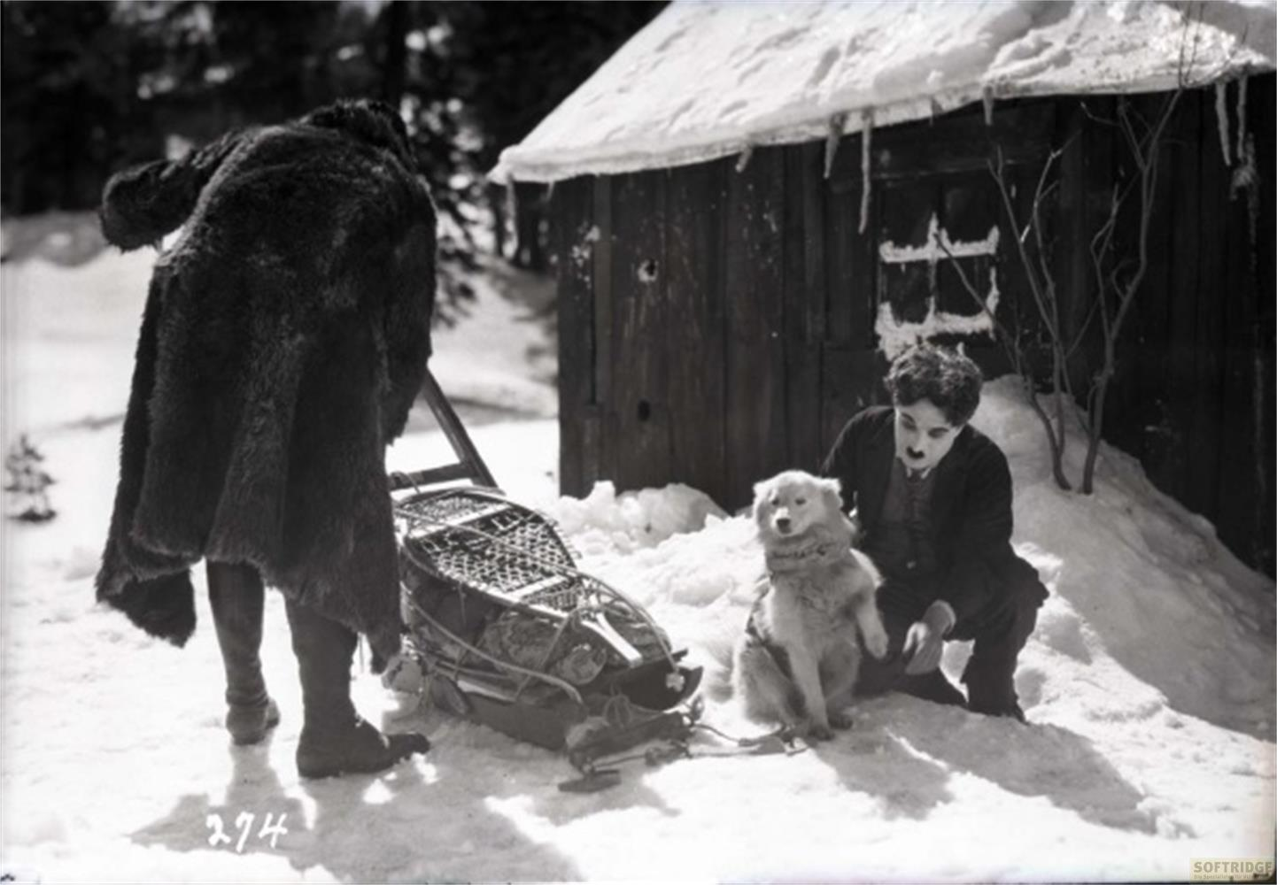 Uomo con cane e slitta nella neve fuori da una capanna.