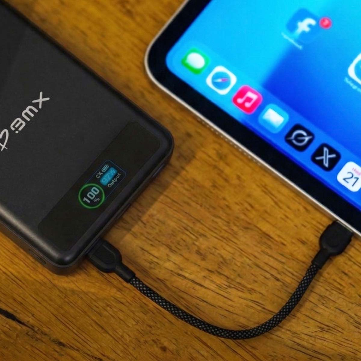 Eine schwarze Powerbank, voll aufgeladen, ist mit einem Tablet verbunden, das App-Icons anzeigt.