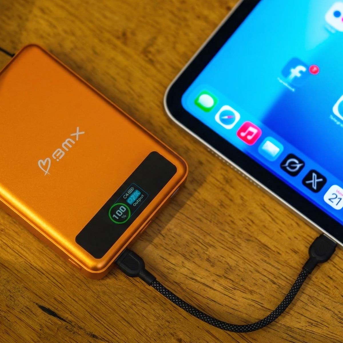Orange Powerbank an Tablet angeschlossen, zeigt 100% Ladung.