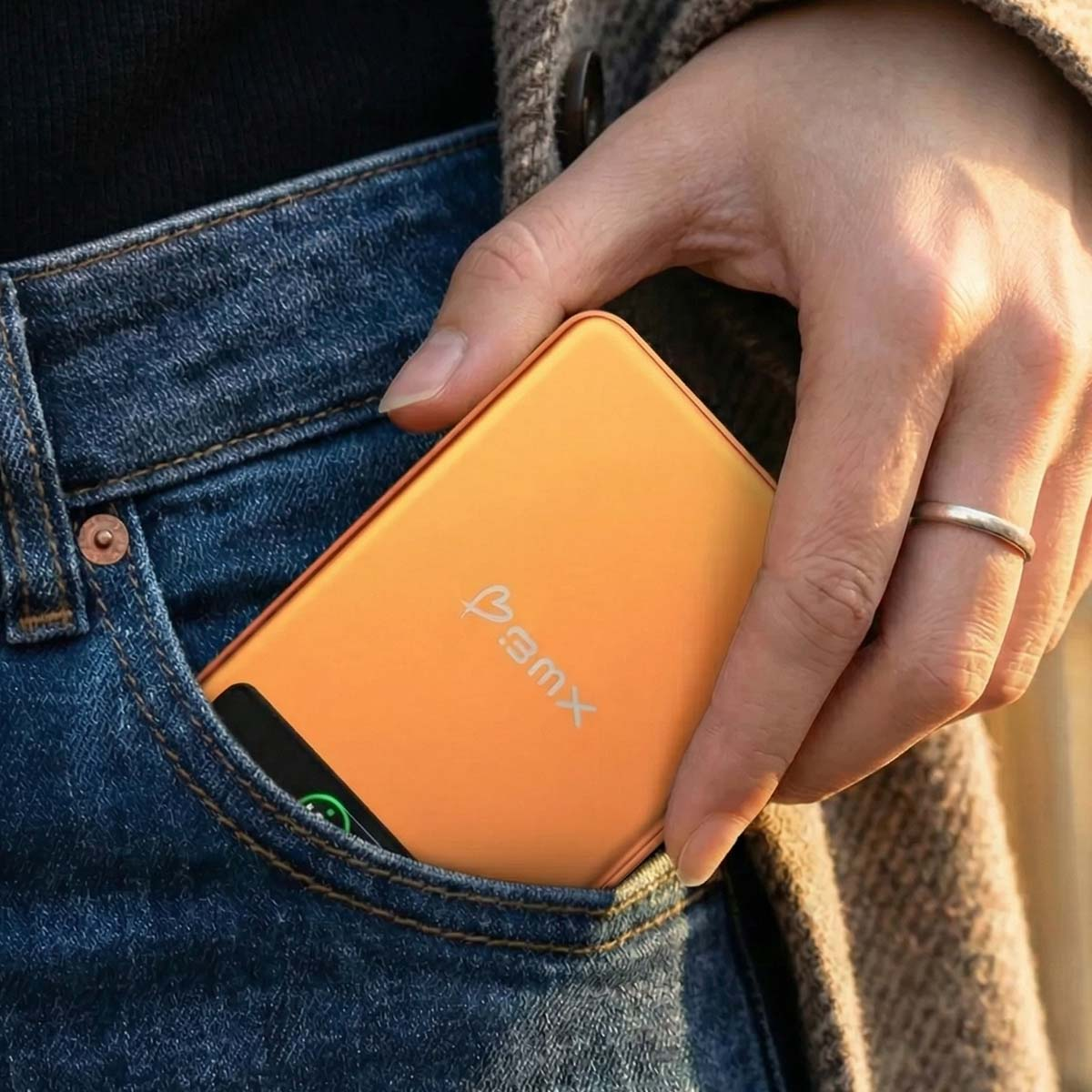 Eine Hand steckt ein oranges Gerät mit Logo in eine Jeans-Hosentasche.