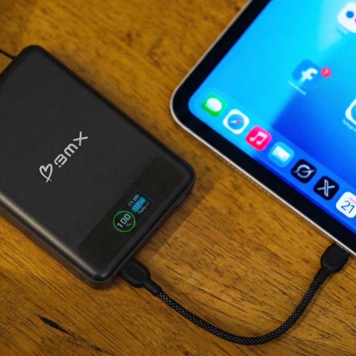 Schwarzes Powerbank lädt Tablet auf einem Holztisch. Anzeige zeigt 100%.