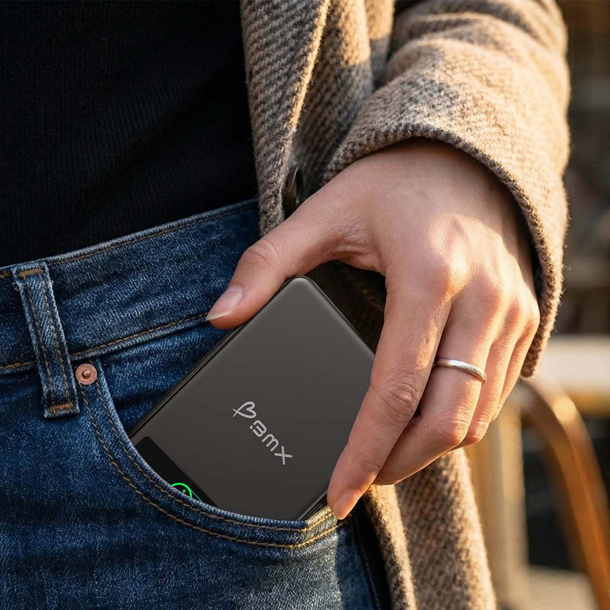 Eine Hand steckt ein schwarzes Ladegerät in eine Jeans-Tasche.