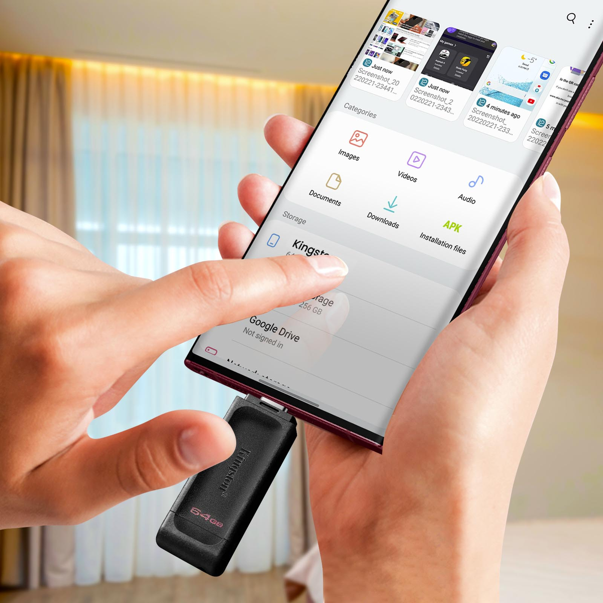 Dłoń trzyma smartfon podłączony do czarnego pendrive'a USB.