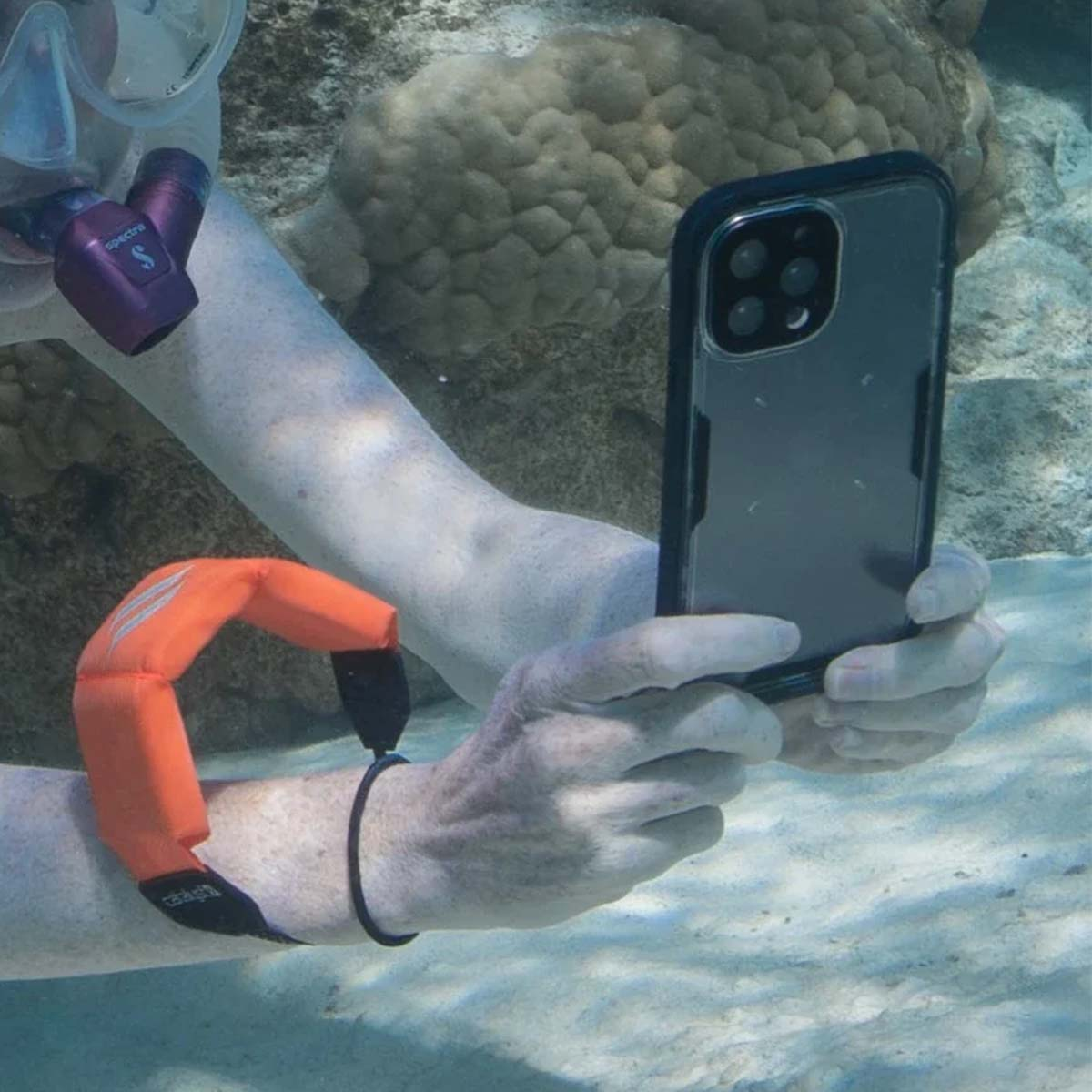 Personne faisant du snorkeling tient téléphone sous l'eau. Flotteur orange au bras.