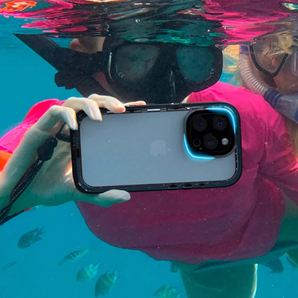 Unterwasseraufnahme: Person mit Schnorchelmaske hält Smartphone vor sich, Fische schwimmen vorbei.