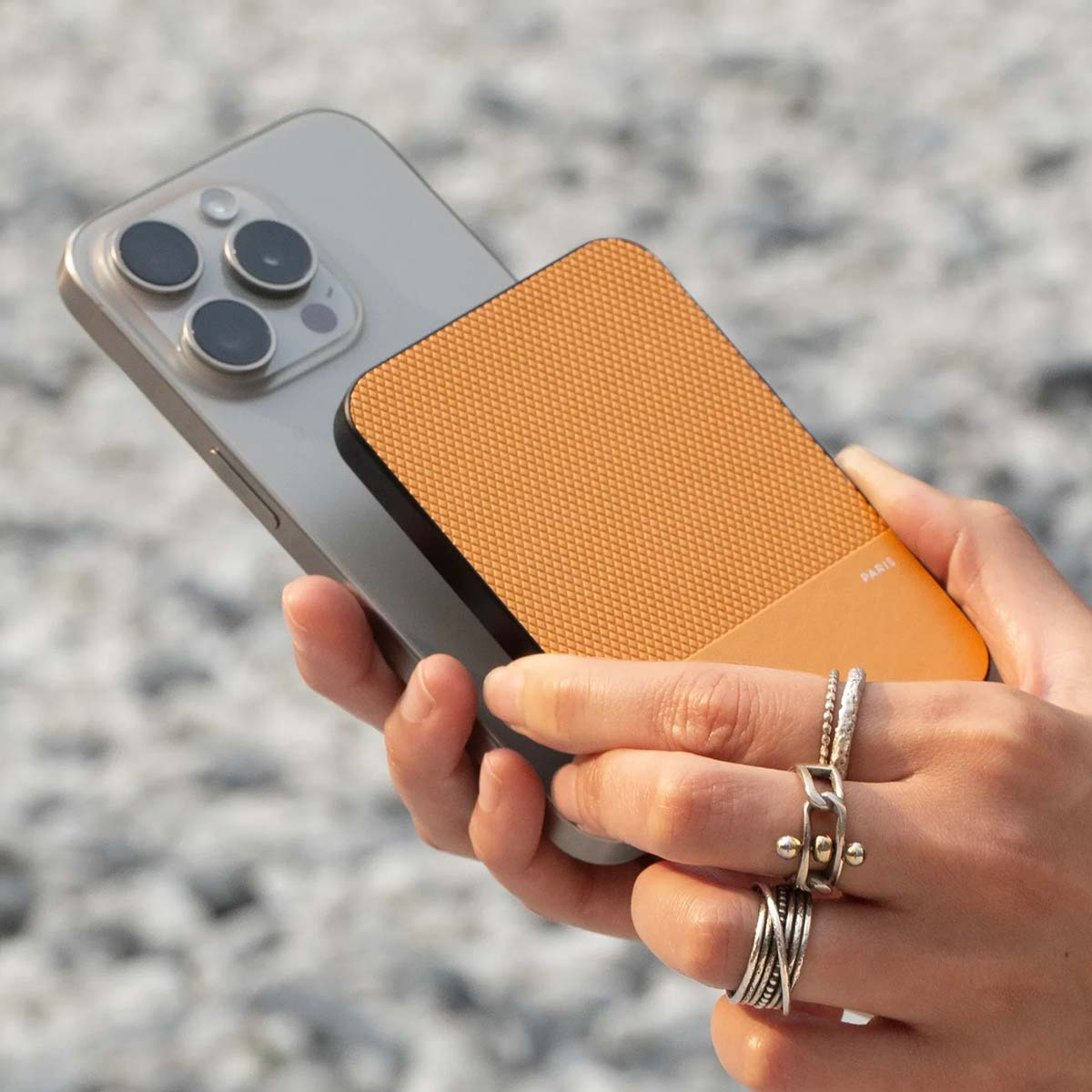 Eine Hand hält ein silbernes Smartphone, an dem ein orangefarbenes Zubehörteil befestigt ist.