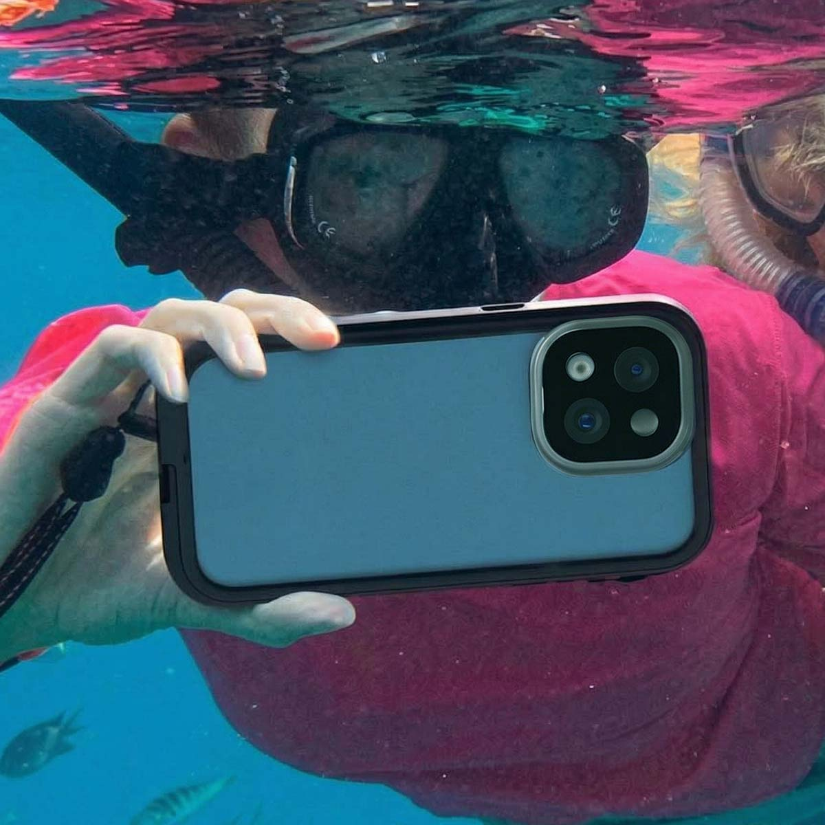 Onderwateropname van een persoon met snorkelmasker die een smartphone vasthoudt. Vissen zijn zichtbaar.