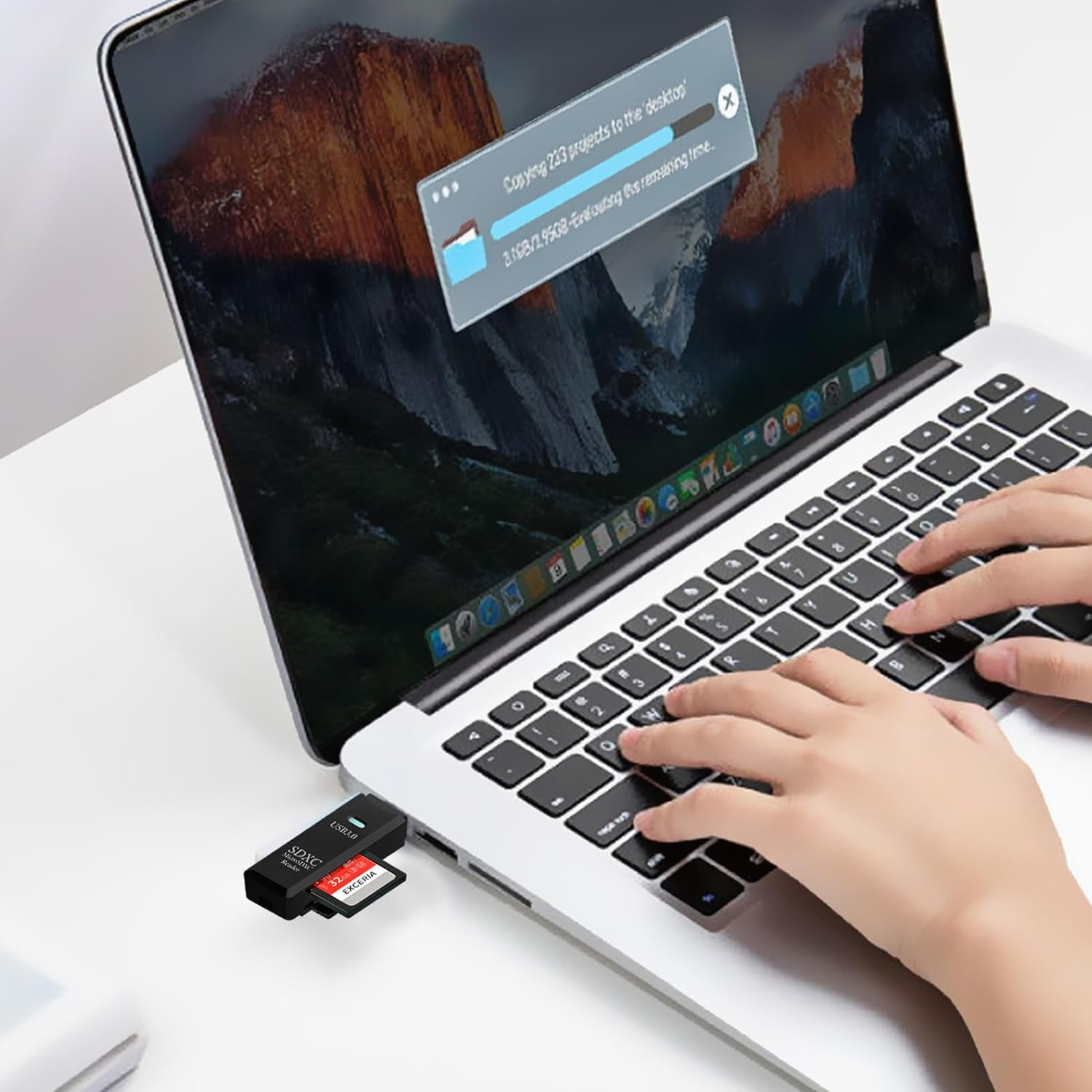 Laptop mit SD-Kartenleser und eingesteckter SDXC-Karte. Hände tippen auf der Tastatur.