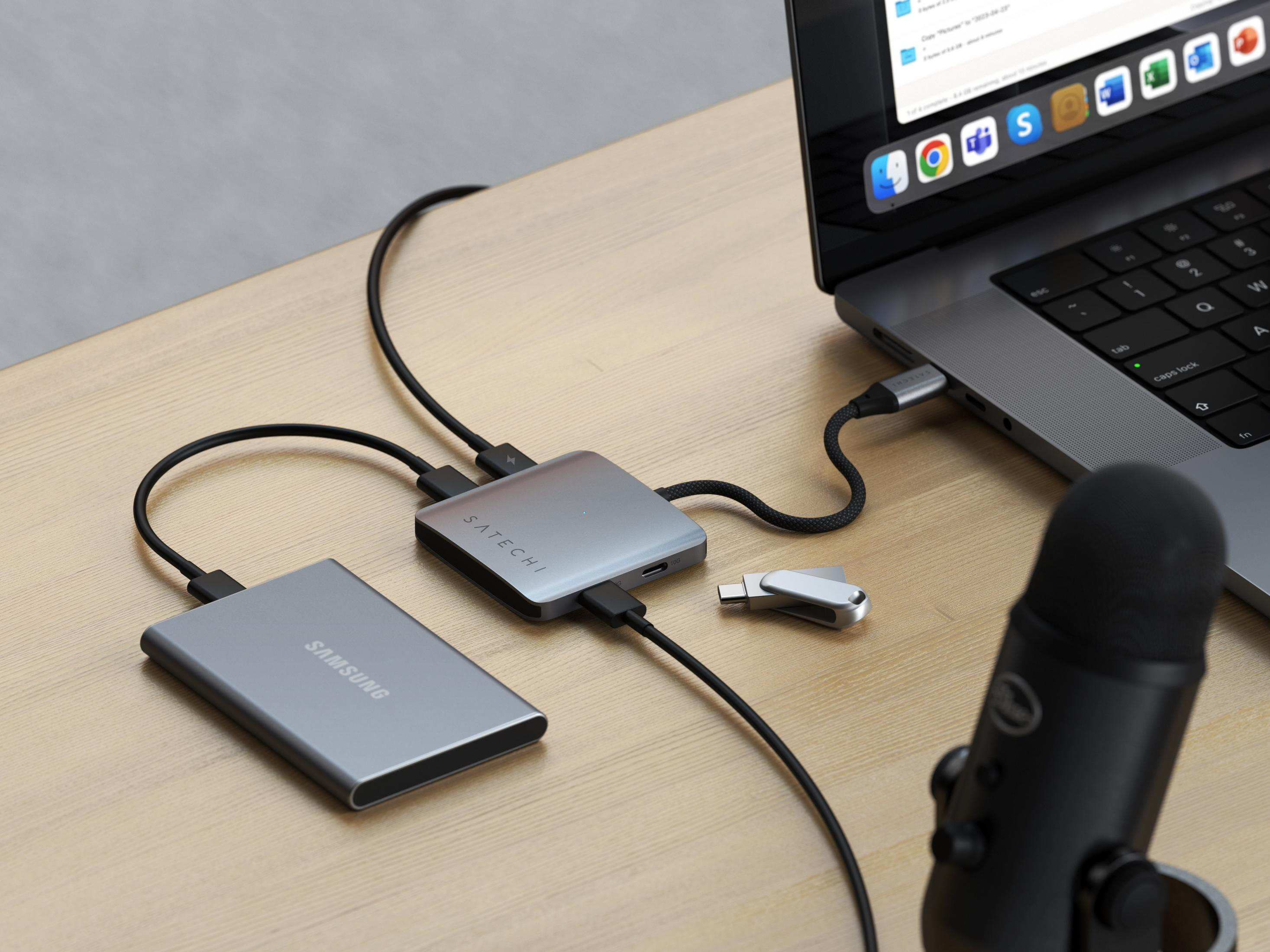 Silberner Laptop, externe Festplatte, Hub, USB-Stick und Mikrofon auf Holztisch.