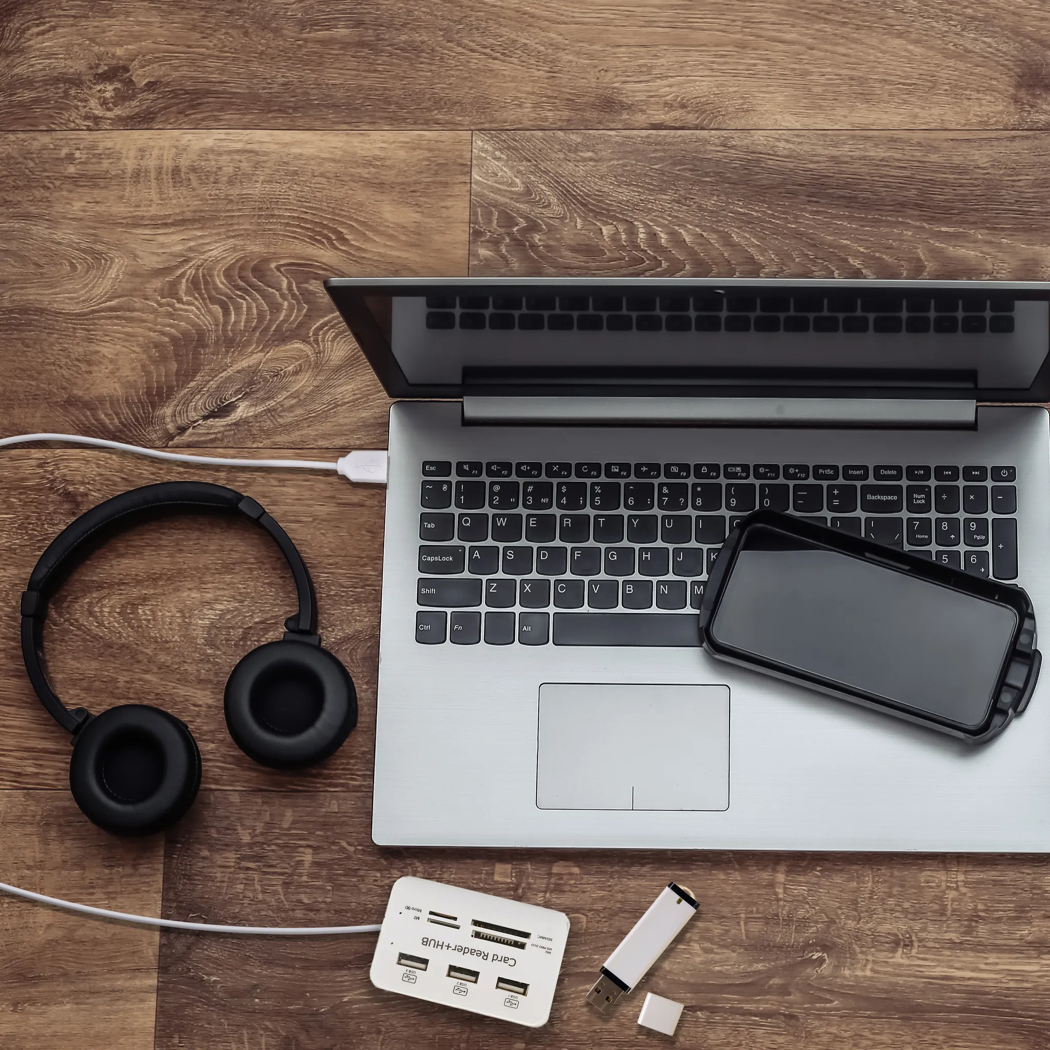 Laptop, Kopfhörer, Smartphone, Kartenleser und USB-Stick auf Holztisch.